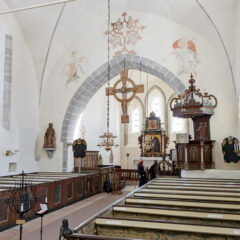 Ett ljust kyrkorum med målade valv, träbänkar och ett stort träkrucifix hängande framför altaret.