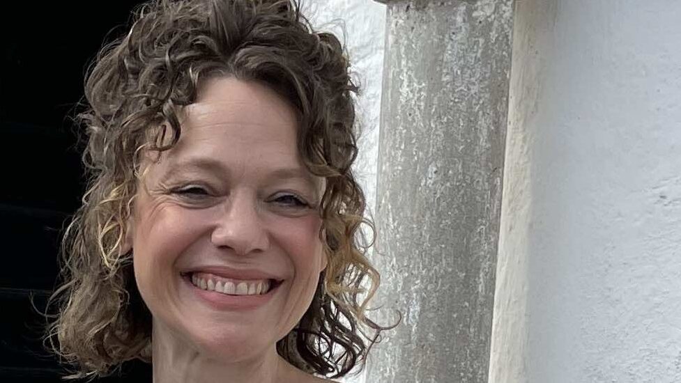 Kvinna med mörkt lockigt uppsatt hår står framför en kalkstensport.