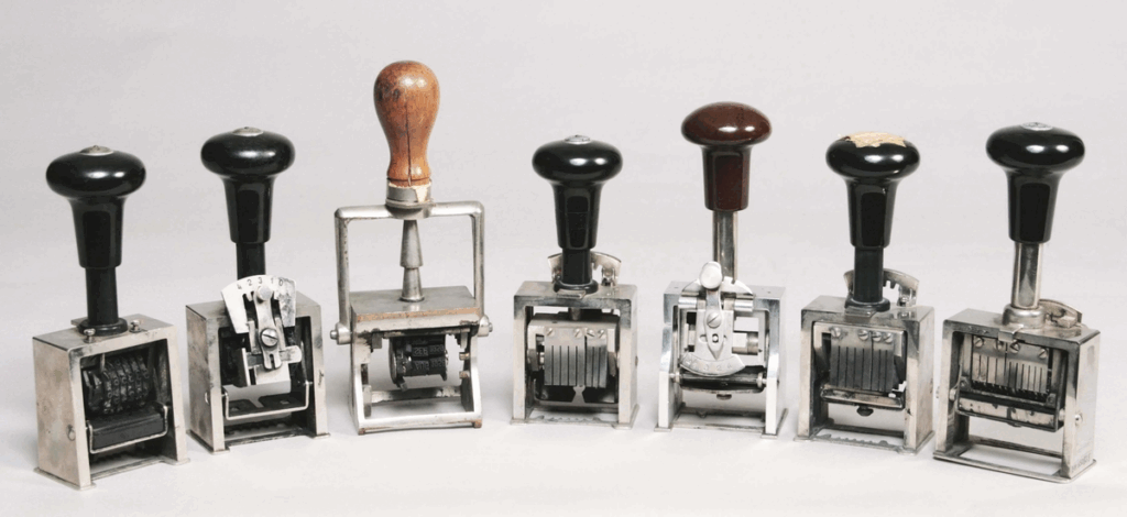 Sju stämplar i metall med träskaft mot vit bakgrund