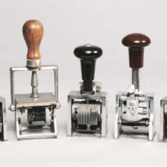 Sju stämplar i metall med träskaft mot vit bakgrund