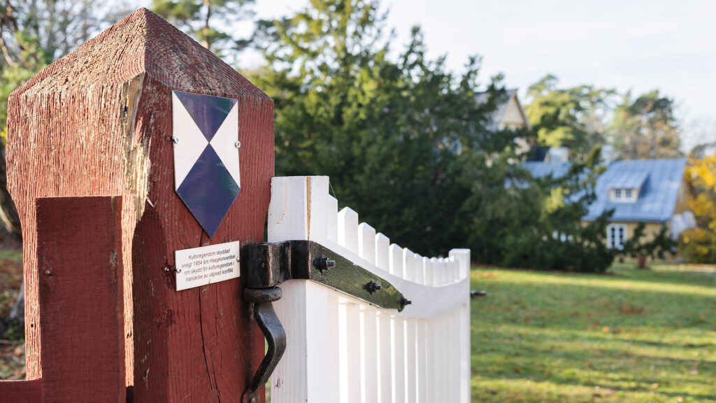 Uppställd och välkomnade vit grind som leder in till ett äldre gult trähus.