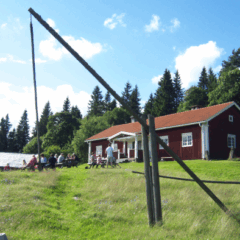 Rödmålat trähus med vita knutar och fönser och med tegeltak står på en grön kulle.