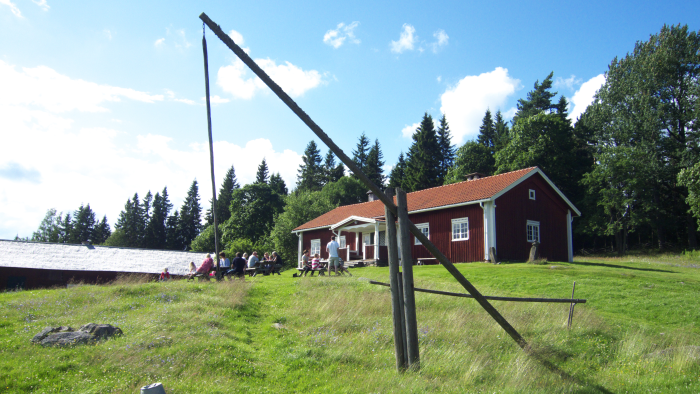 Rödmålat trähus med vita knutar och fönser och med tegeltak står på en grön kulle.