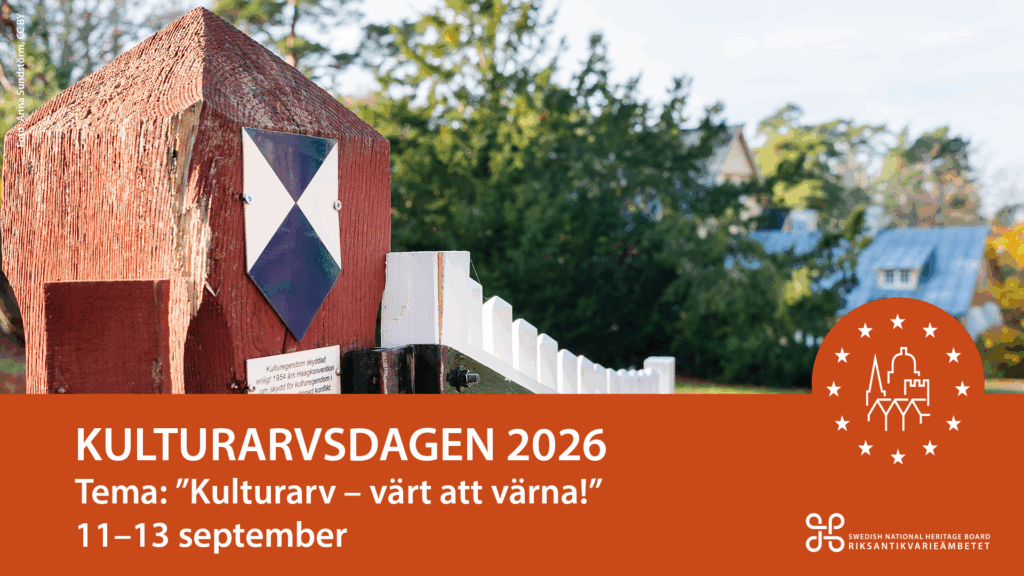 En blåvit skylt sitter på grindstolpen vid en uppställd välkomnade vit trägrind som leder in till ett äldre gult trähus.