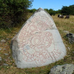 Grå stor sten med röda runor, ligger i en hage med grönt gräs och får.