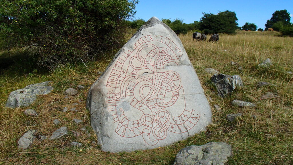 Grå stor sten med röda runor, ligger i en hage med grönt gräs och får.