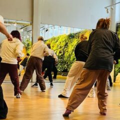 Ungdomar med säckiga kläder dansar med ryggarna mot kameran i en ljus danssal.