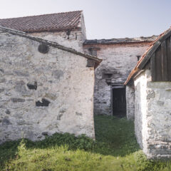 Murade, vitkalkade och slitna gamla hus i olika storlekar som sitter ihop med mur. I mitten en ingång med en sned trädörr.