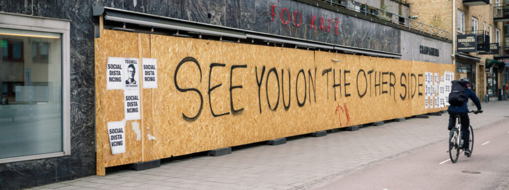 En person cyklar förbi ett högt träplank med där det står skrivet med svart See you on the other side