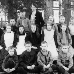 Skolelever i finkläder är uppställda för skolfotografering men lärarinnan stående längst bak.