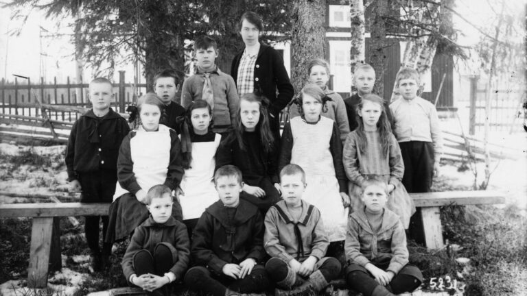 Skolelever i finkläder är uppställda för skolfotografering men lärarinnan stående längst bak.