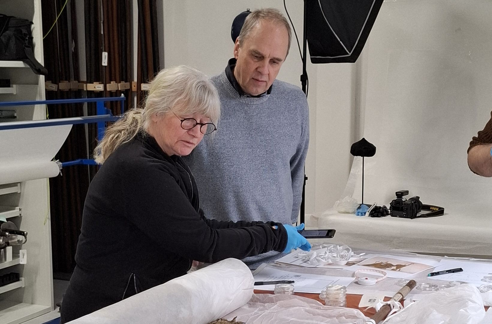 Gråhårg man och kvinnan står vid bord och tittar på vit tygrulle