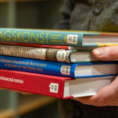En bokhög där bokryggarna syns. Högen hålls av händer.