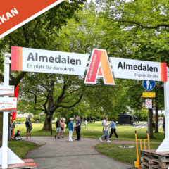 Vy över Almedalsparken med stora gröna träd i bakgrunden och några bodar för besökare längs gångstigar.