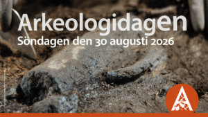 Närbild på arkeologiskt fynd, en slags kanna som ligger halvt dold i jorden. På bilden ligger text med datum samt en symbol i orange.