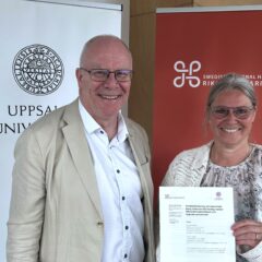 Två leende personer står framför rollups från Uppsala universitet och Riksantikvarieämbetet; den ena håller upp ett dokument om samarbete inom kulturarvsforskning.