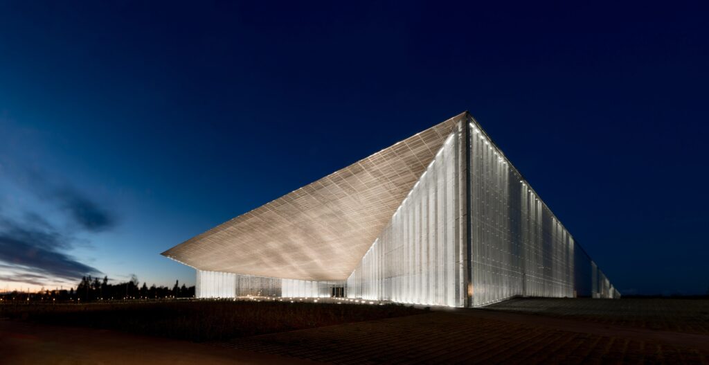 Det moderna huvudbyggnaden för Estlands nationalmuseum i Tartu med en lång, vinklad byggnadskropp och glasfasad. Byggnaden är upplyst och lyser i mörkret.