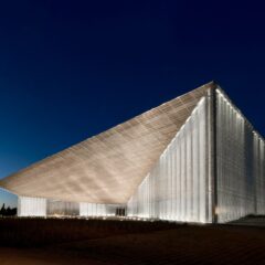 Det moderna huvudbyggnaden för Estlands nationalmuseum i Tartu med en lång, vinklad byggnadskropp och glasfasad. Byggnaden är upplyst och lyser i mörkret.