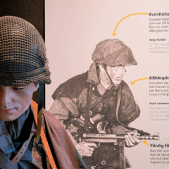 En skyltdocka iklädd militärkläder och hjälm står framför en plansch med bilder och förklaringar på utrustningen.