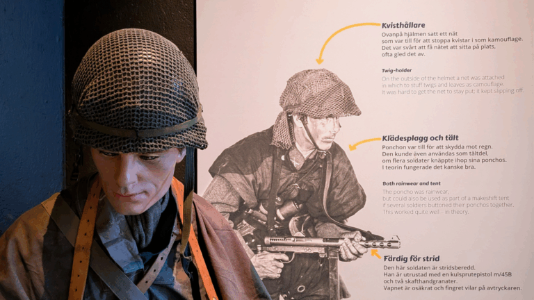 En skyltdocka iklädd militärkläder och hjälm står framför en plansch med bilder och förklaringar på utrustningen.