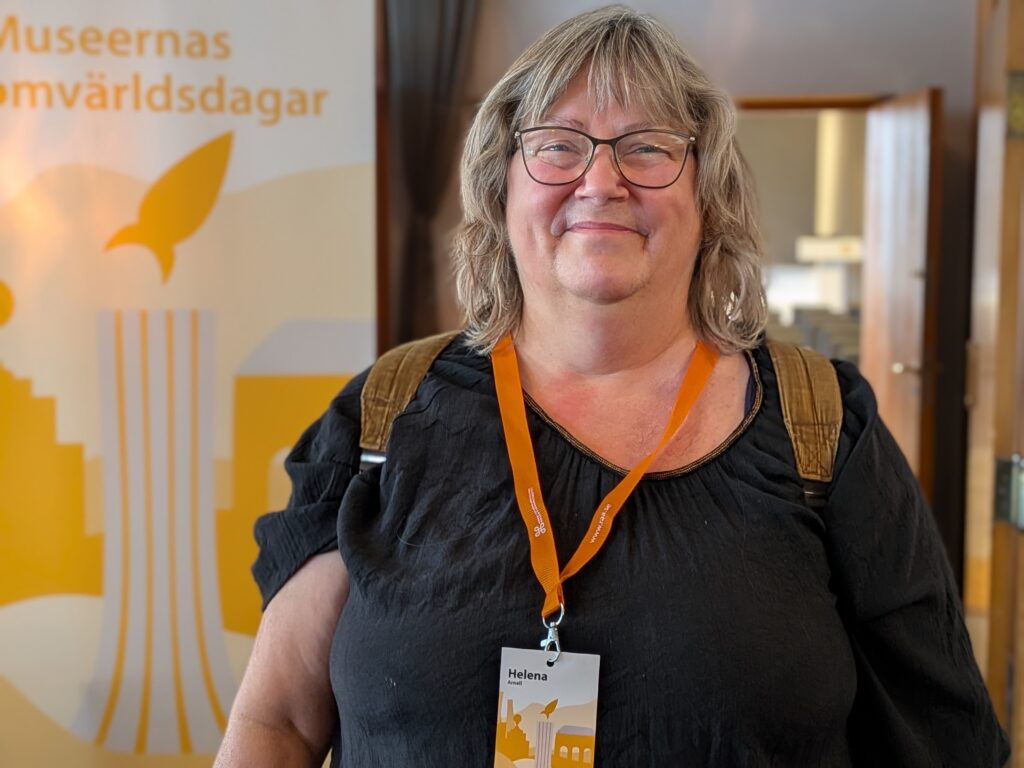Kvinna med glasögon står framför en vepa med texten Museernas omvärldsdagar.
