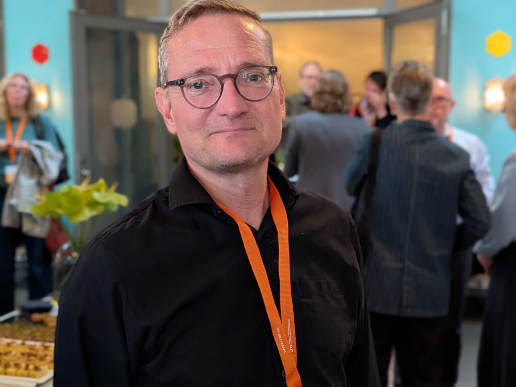 Man med glasögon och svart skjorta ser in i kameran.