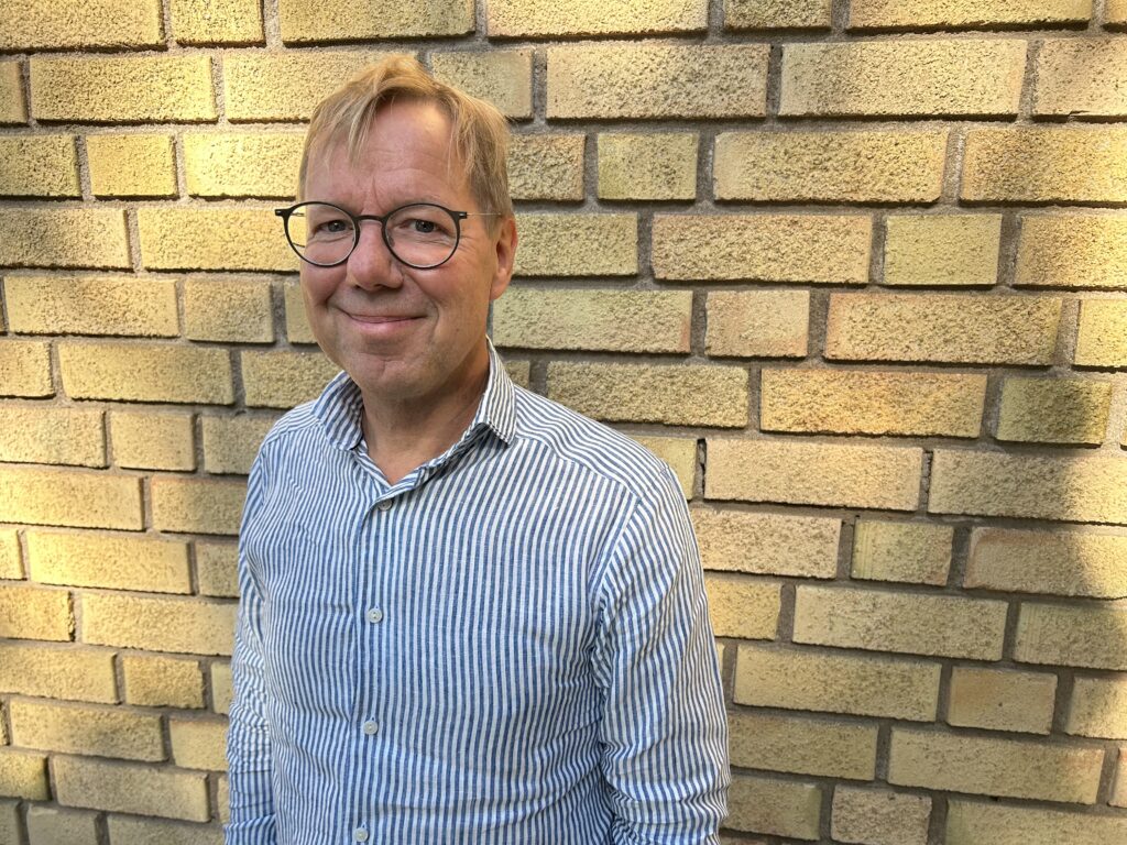 Man med glasögon framför tegelvägg