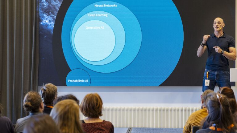 En man står på en scen och föreläser inför publik.