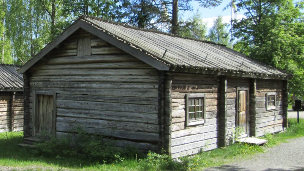Mörkt trähus framför gröna träd